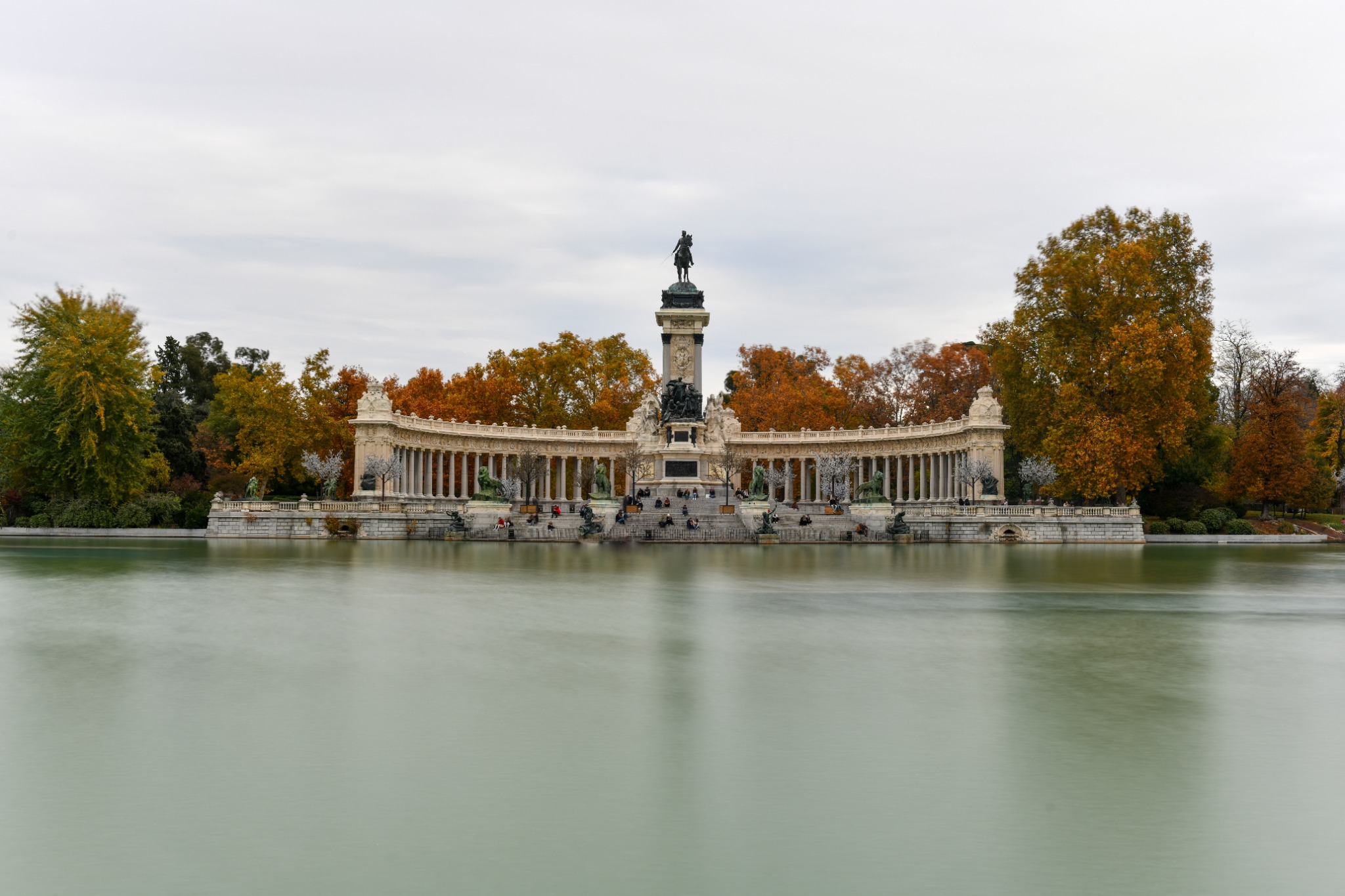 Monument to Alfonso XII across the lake in El Retiro Park, Madrid, surrounded by autumn trees.