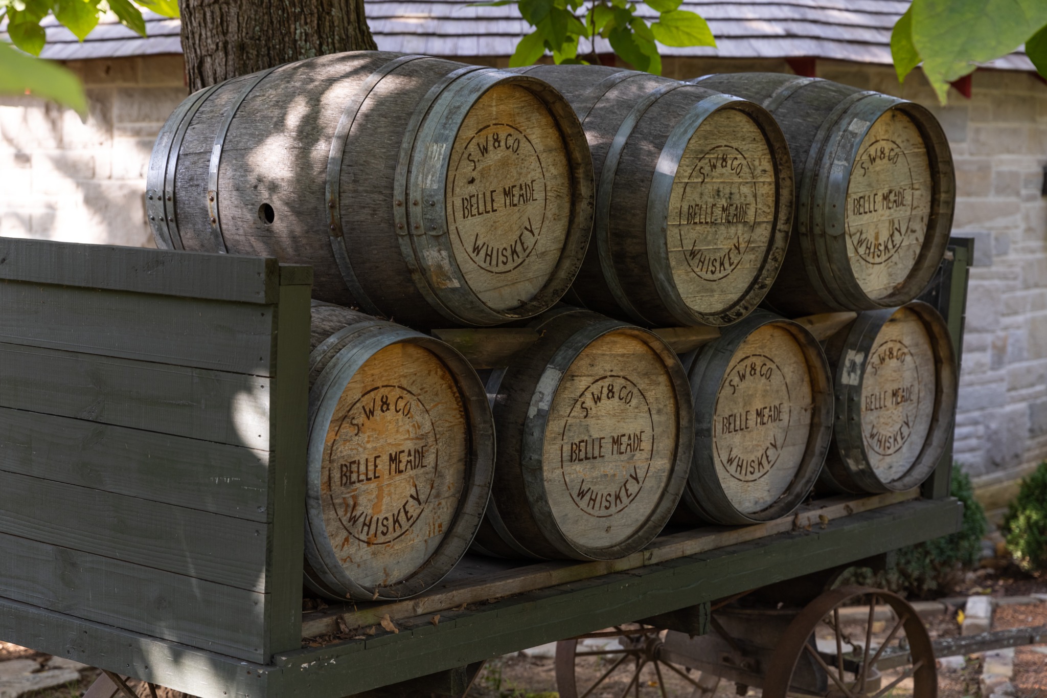 A close view of weathered Belle Meade whiskey barrels stacked on a wooden wagon beneath shade trees at the historic Belle Meade property in Nashville, Tennessee. Alternative text: Wooden Belle Meade whiskey barrels stacked on a wagon beneath leafy trees in Nashville, Tennessee. Title: Belle Meade Whiskey Barrels in Nashville Caption: Historic Belle Meade whiskey barrels displayed on a wooden wagon in Nashville. Description: A close view of weathered Belle Meade whiskey barrels stacked on a wooden wagon beneath shade trees at the historic Belle Meade property in Nashville, Tennessee. Keywords: Nashville, Belle Meade, whiskey barrels, Tennessee, historic attraction