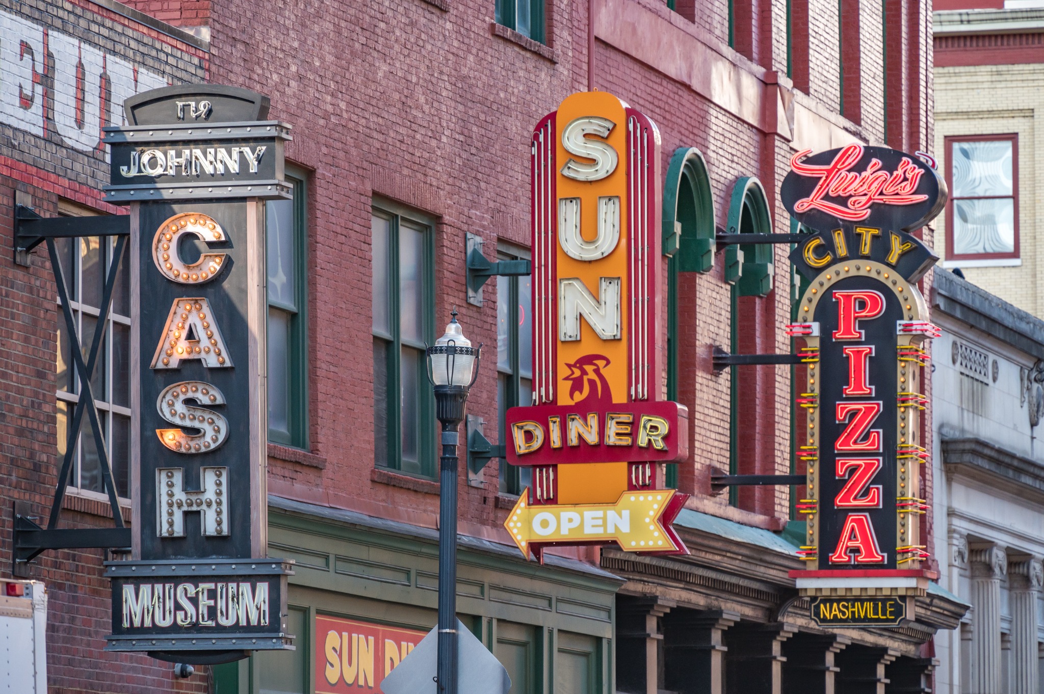 A streetscape of colorful neon signs in downtown Nashville, including the Johnny Cash Museum, Sun Diner, and Luigi's City Pizza. Alternative text: Vintage neon signs for the Johnny Cash Museum, Sun Diner, and Luigi's City Pizza in downtown Nashville. Title: Neon Signs in Downtown Nashville Caption: Colorful vintage-style neon signs in Nashville's downtown entertainment district. Description: A streetscape of colorful neon signs in downtown Nashville, including the Johnny Cash Museum, Sun Diner, and Luigi's City Pizza. Keywords: Nashville, neon signs, downtown Nashville, Broadway, Johnny Cash Museum