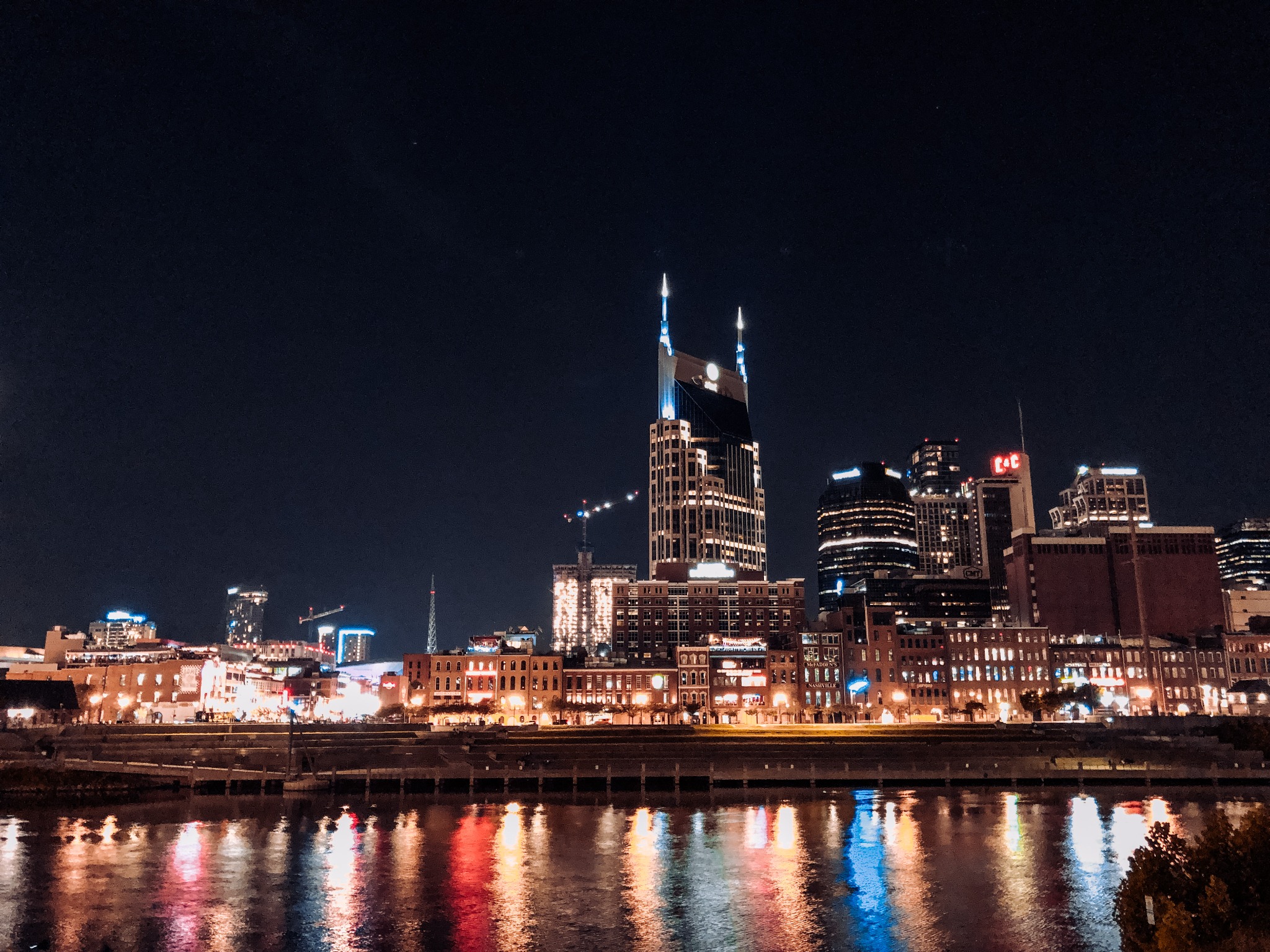 A nighttime view of downtown Nashville from across the Cumberland River, with city lights creating colorful reflections on the water. Alternative text: Downtown Nashville skyline glowing at night with colorful reflections on the Cumberland River. Title: Downtown Nashville Skyline at Night Caption: Nashville's illuminated downtown skyline reflected in the Cumberland River. Description: A nighttime view of downtown Nashville from across the Cumberland River, with city lights creating colorful reflections on the water. Keywords: Nashville skyline, downtown Nashville, Cumberland River, Nashville at night, Tennessee