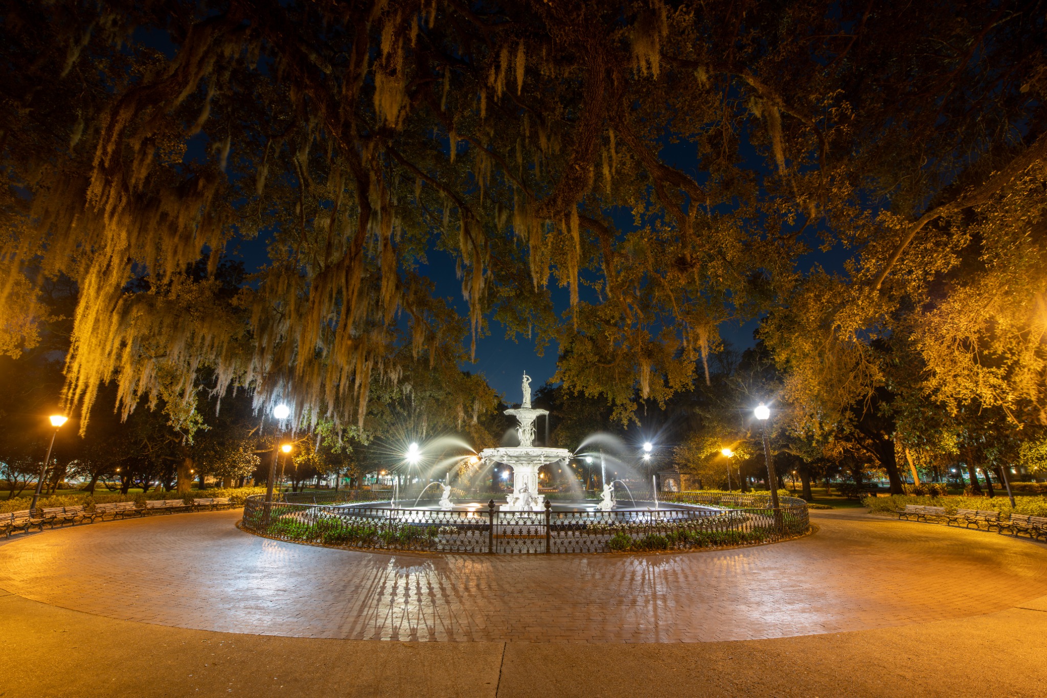 Warm lights illuminate the Forsyth Park fountain and moss-draped live oaks after dark in Savannah.