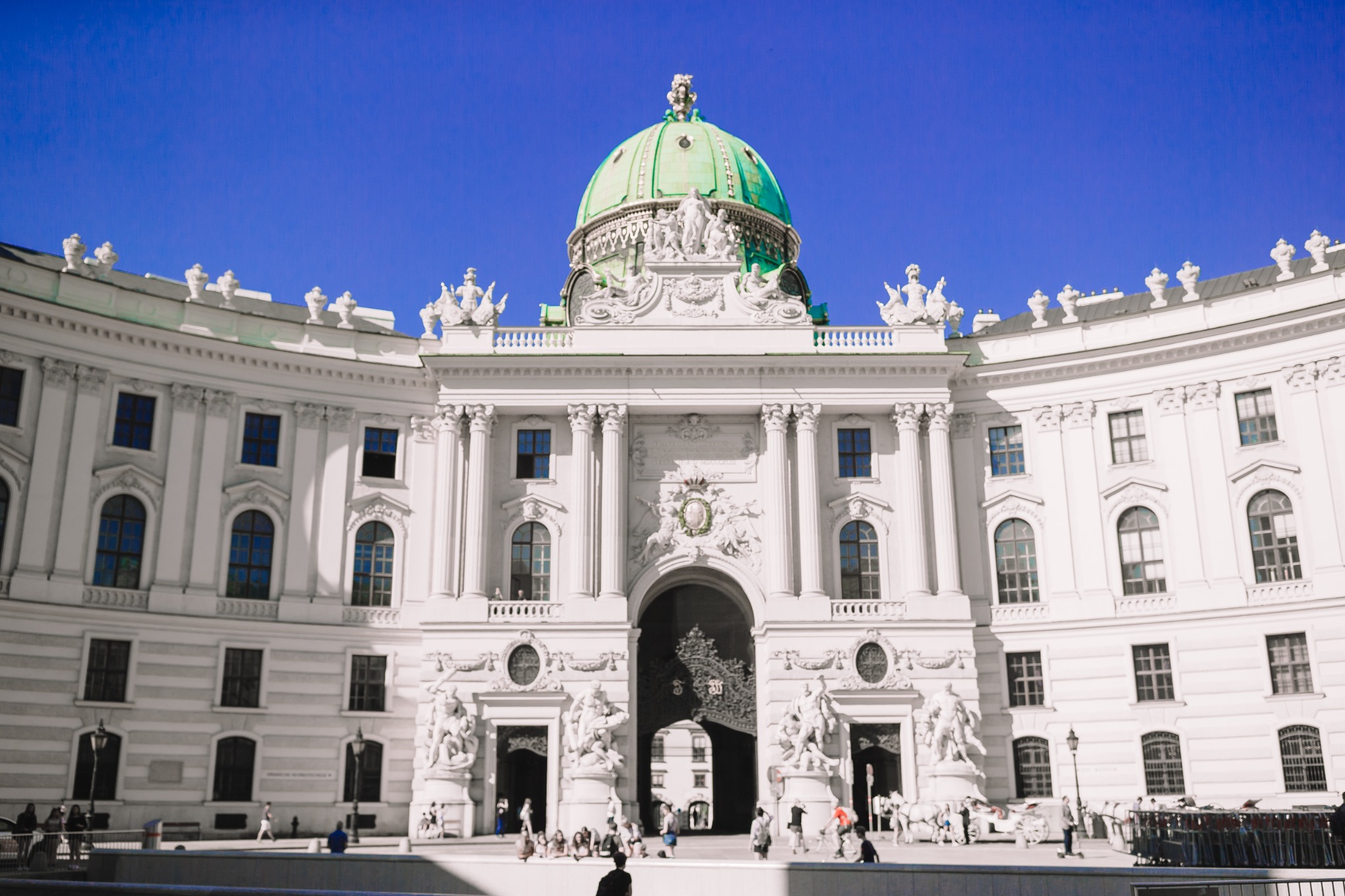 Detailed daytime view of Vienna’s Hofburg Palace at Michaelerplatz, featuring the white Baroque façade, sculpted entrance and prominent green dome.