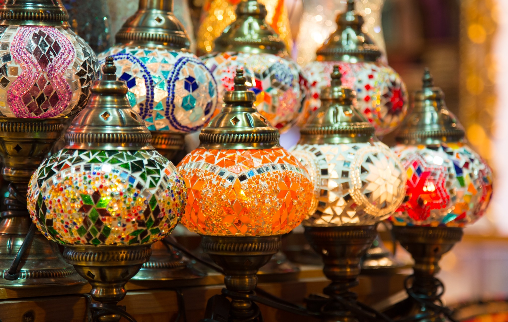 Colorful handmade Turkish mosaic lamps displayed together in an Istanbul market. A close-up photograph of ornate Turkish mosaic lamps in vivid orange, green, blue, red, and white glass, displayed in a market or bazaar in Istanbul, Turkey.