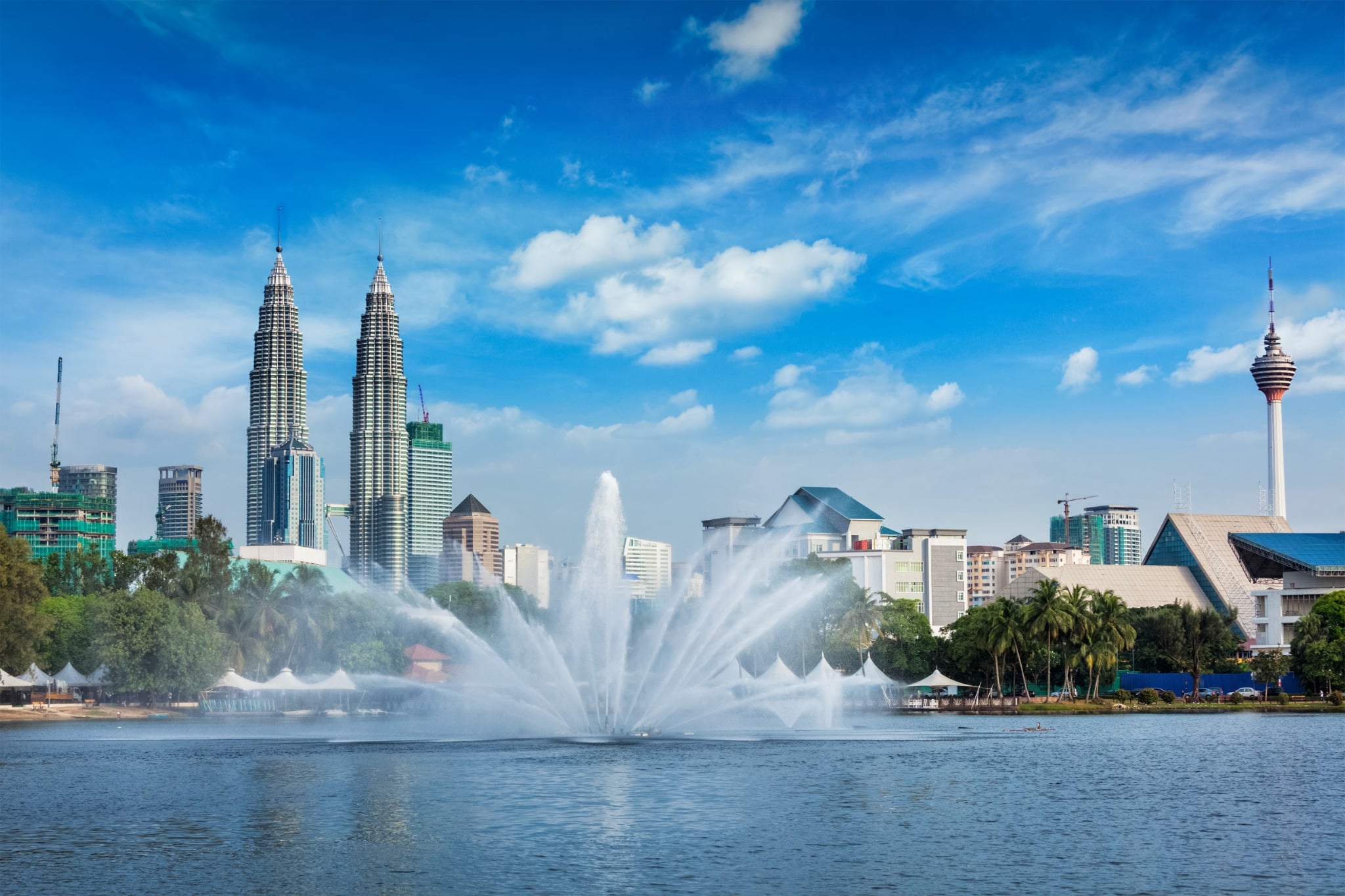 A lake fountain frames the Petronas Twin Towers and KL Tower on Kuala Lumpur's skyline.