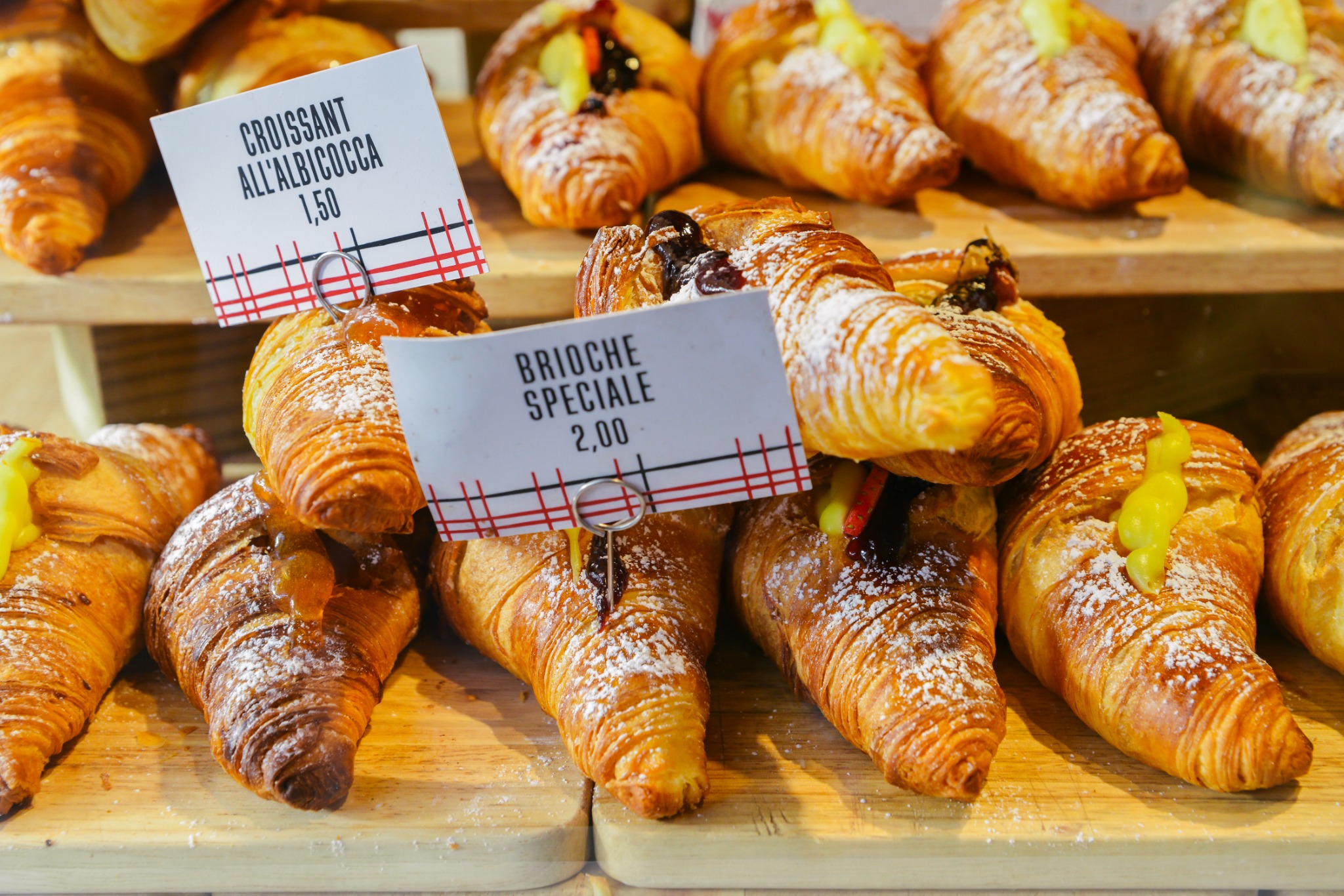 Close-up food image of assorted Italian pastries, including croissants and filled brioches, displayed at a traditional Milan bakery.