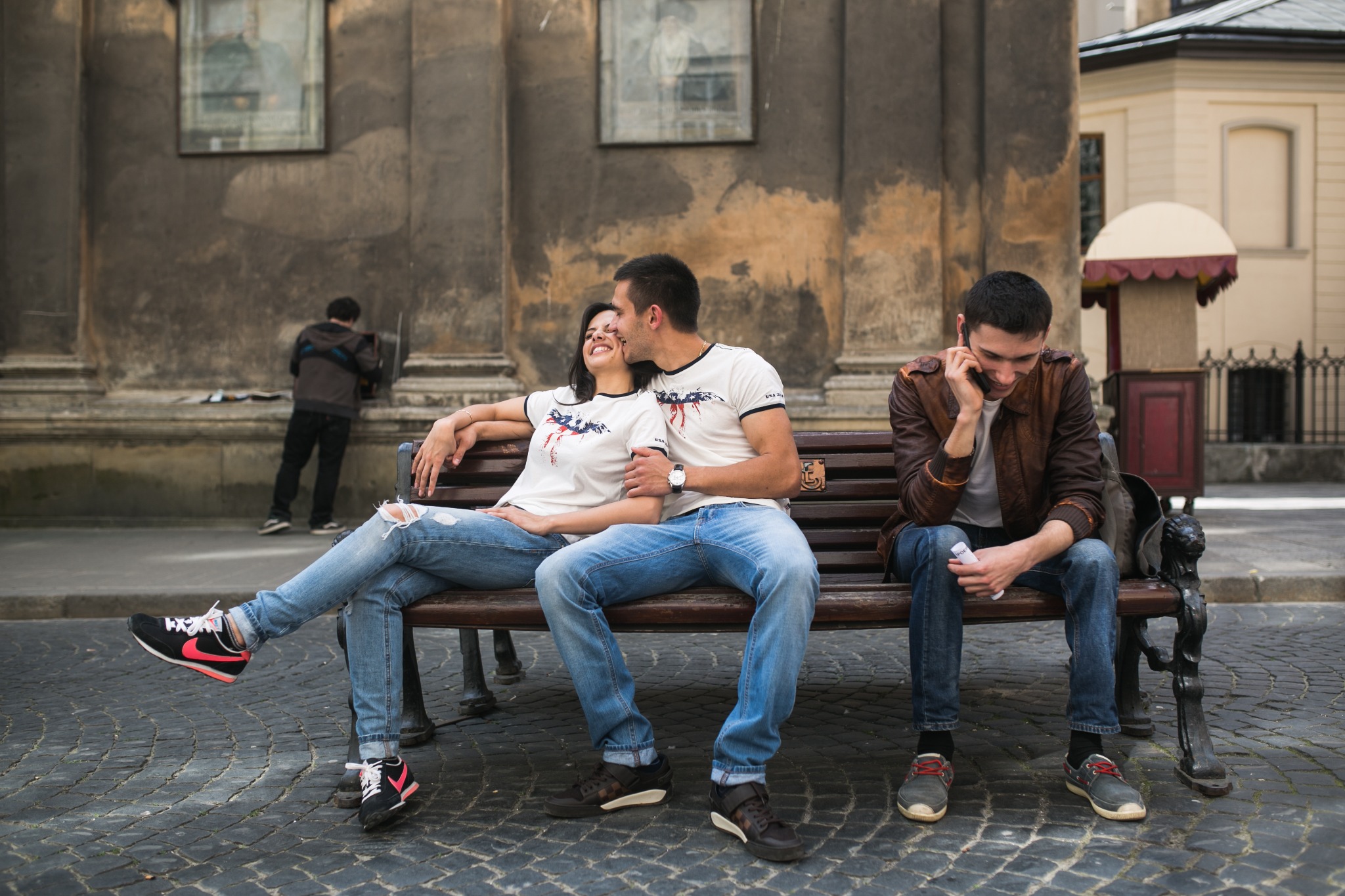 Travel lifestyle image of a couple relaxing on a public bench during a city break in Milan, suitable for hotel, sightseeing, and romantic getaway content.