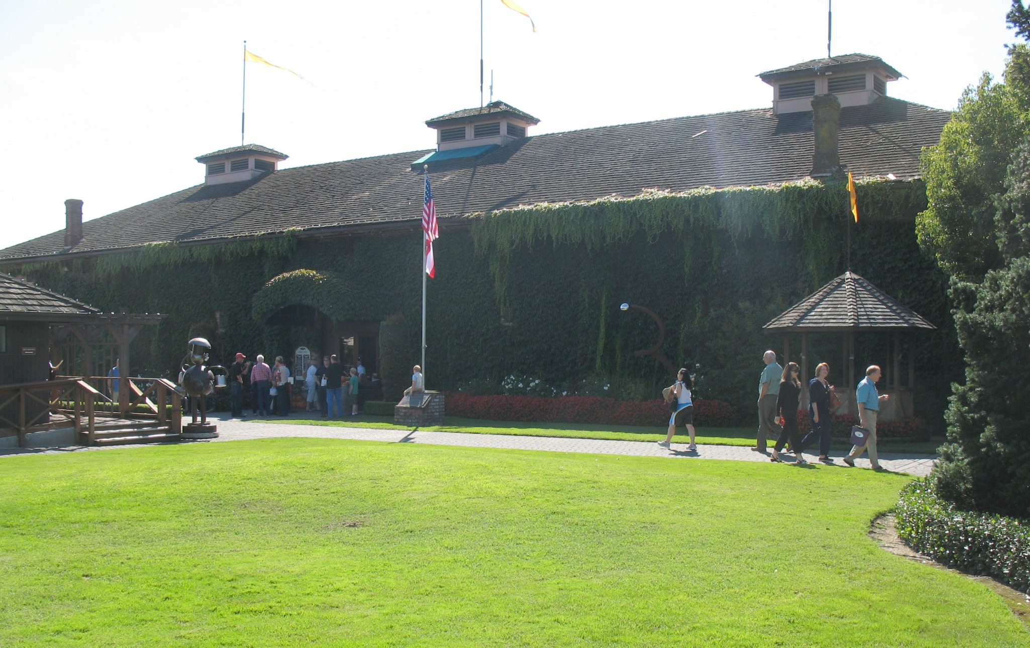 A view of the ivy-covered historic Groezinger Wine Cellars building in Yountville, California, with visitors walking across the landscaped grounds in Napa Valley. Alternative text: Historic Groezinger Wine Cellars building in Yountville, Napa Valley, with visitors on the lawn. Title: Historic Groezinger Wine Cellars in Yountville Caption: The historic Groezinger Wine Cellars complex in Yountville, Napa Valley. Description: A view of the ivy-covered historic Groezinger Wine Cellars building in Yountville, California, with visitors walking across the landscaped grounds in Napa Valley.