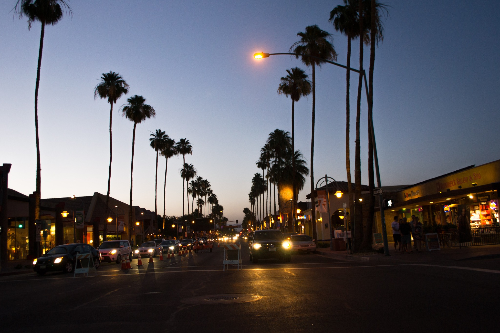 Palm Canyon Drive at dusk with palm trees, traffic and illuminated shops in Palm Springs
