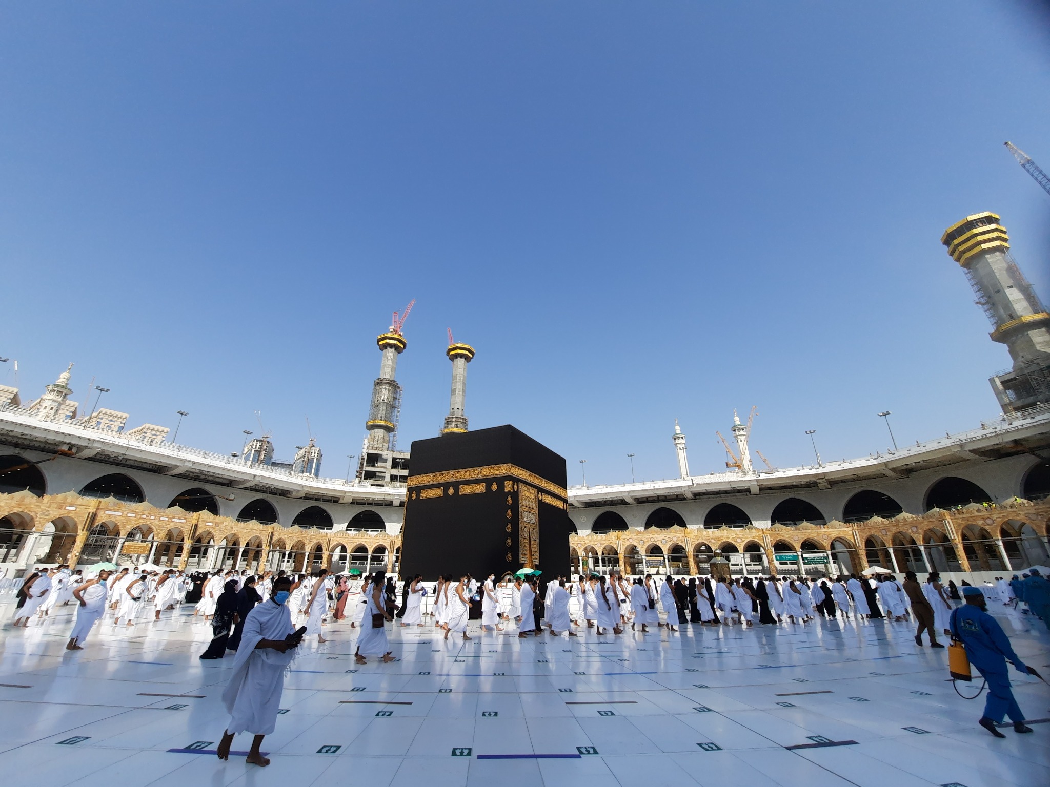 Alternative text: Pilgrims performing tawaf around the Kaaba in the courtyard of Masjid al-Haram. Title: Pilgrims Performing Tawaf Around the Kaaba Caption: Pilgrims circle the Kaaba during tawaf at Masjid al-Haram in Mecca. Description: Wide daytime view of pilgrims performing tawaf around the Kaaba at Masjid al-Haram in Mecca. The white marble courtyard, mosque arches, minarets, and construction towers surround the sacred site. Wide daytime view of pilgrims performing tawaf around the Kaaba at Masjid al-Haram in Mecca. The white marble courtyard, mosque arches, minarets, and construction towers surround the sacred site.
