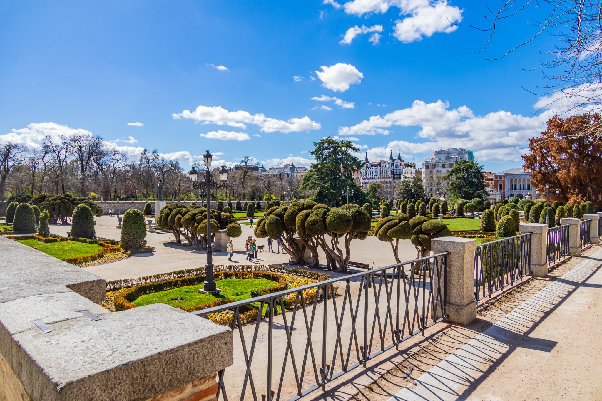 Formal gardens, sculpted trees, and walking paths in El Retiro Park, Madrid, beneath a bright blue sky.