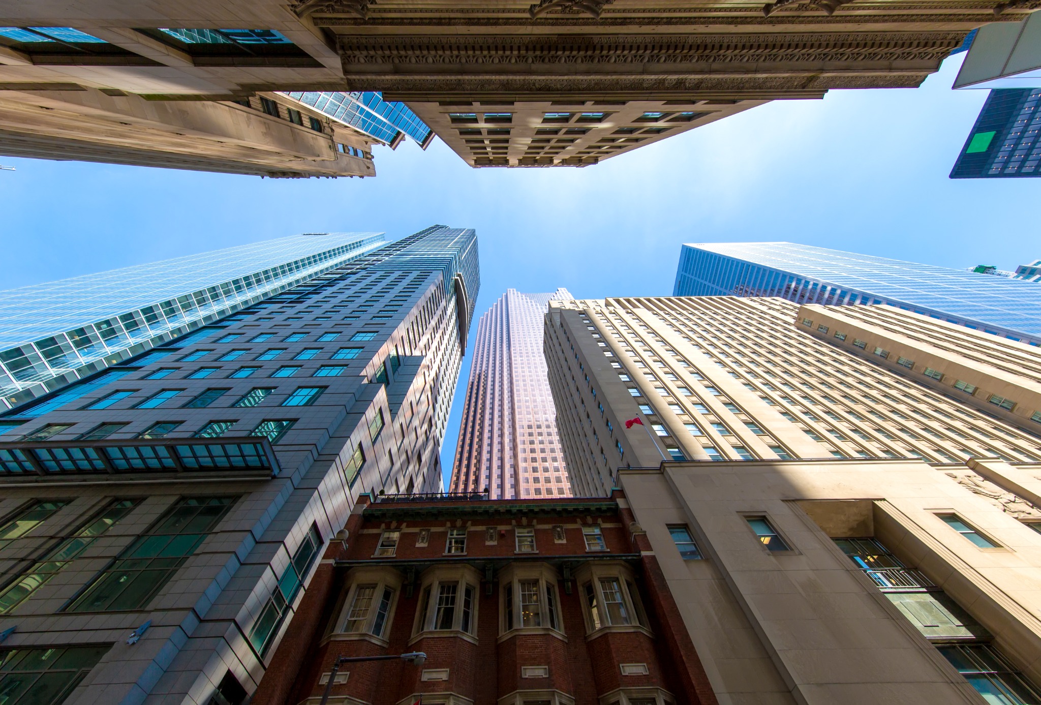 An upward architectural view among the skyscrapers of Toronto's Financial District. Modern glass and stone office towers surround a smaller historic building in the downtown core.